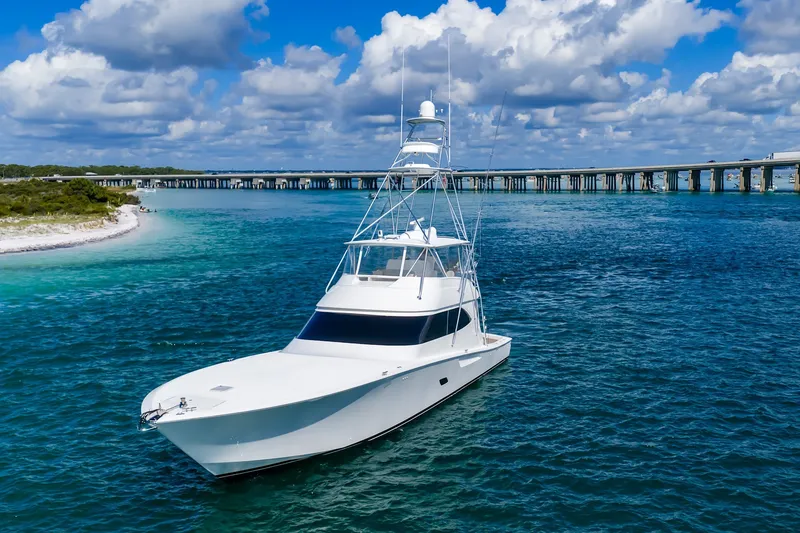 Slide: The Image of 2012 Viking 76 Convertible yacht cruising in clear blue waters near a bridge. - 3