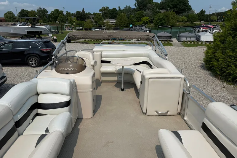 Slide: The Image of 2008 Manitou Oasis pontoon boat with white seating and helm, parked near a marina. - 10