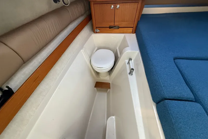 Slide: The Image of 2005 Glacier Bay 2685 Coastal Runner interior with compact marine toilet and blue seating. - 13