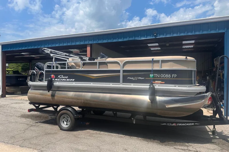 The Image of 2023 Sun Tracker Party Barge 18 DLX pontoon boat on trailer, parked outside a garage. - 0