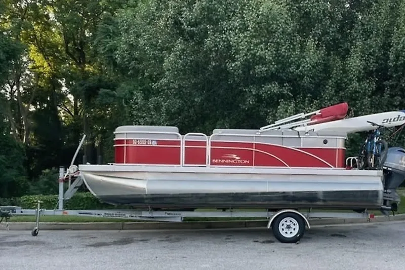 Slide: The Image of 2021 Bennington 205E pontoon boat on trailer, parked near lush greenery. - 1