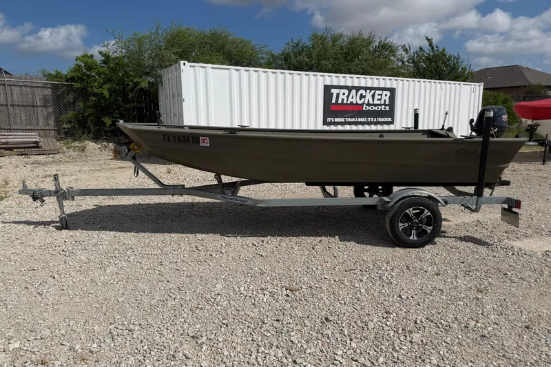 The Image of 2004 SeaArk 1448 MV boat on trailer, parked outdoors near Tracker Boats container. - 0
