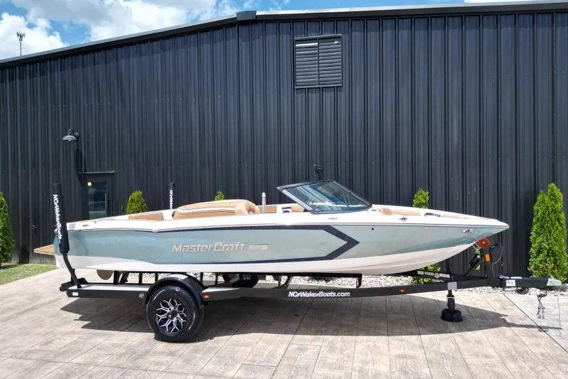 The Image of 2023 MasterCraft ProStar boat on trailer, parked outside a black building. - 1