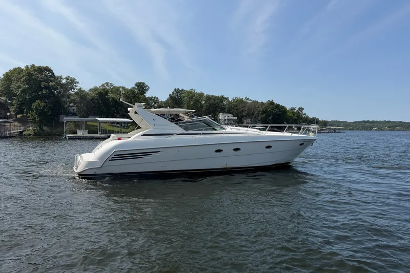 Slide: The Image of 1997 Trojan 440 Express yacht cruising on a serene lake with lush green shoreline. - 5