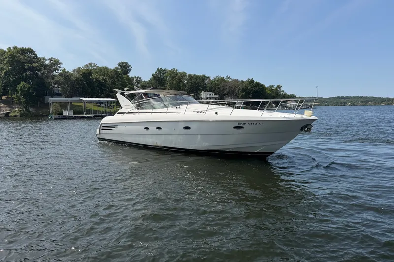 Slide: The Image of 1997 Trojan 440 Express yacht on a serene lake with lush green shoreline. - 3