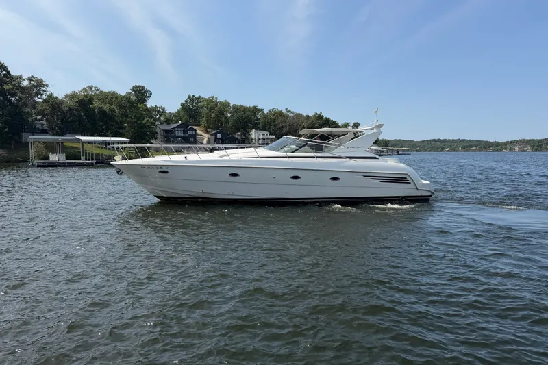 The Image of 1997 Trojan 440 Express yacht cruising on a serene lake under a clear blue sky. - 0