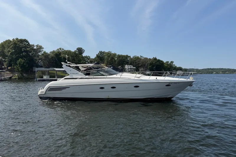 Slide: The Image of 1997 Trojan 440 Express yacht on a serene lake with lush green shoreline. - 4