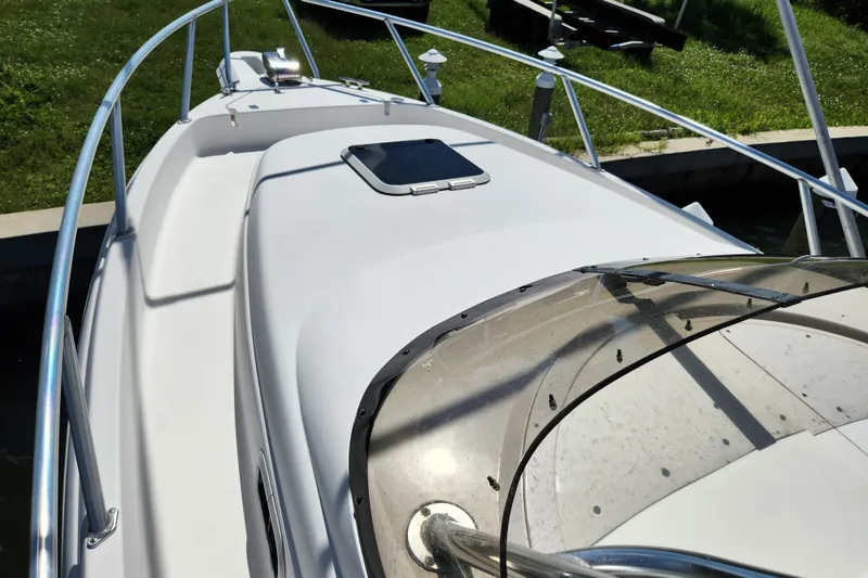 Slide: The Image of 2003 Intrepid 289 Walkaround boat deck with railing and hatch, docked near grassy area. - 20