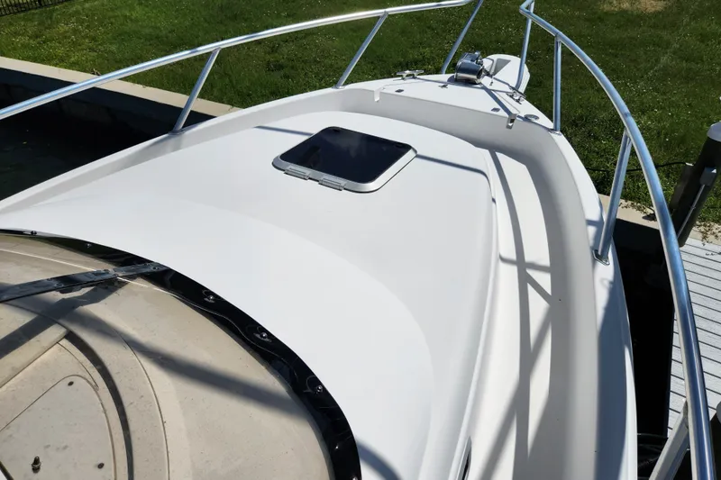 Slide: The Image of 2003 Intrepid 289 Walkaround boat deck with railing and hatch, docked near grassy area. - 23