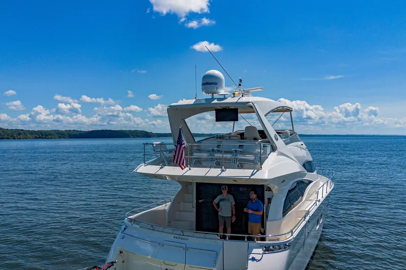 Slide: The Image of 2004 Marquis 59 yacht on open water with two people onboard, clear blue sky. - 16