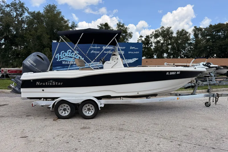 The Image of 2016 NauticStar 211 Angler boat on trailer, parked outdoors under a blue sky. - 0