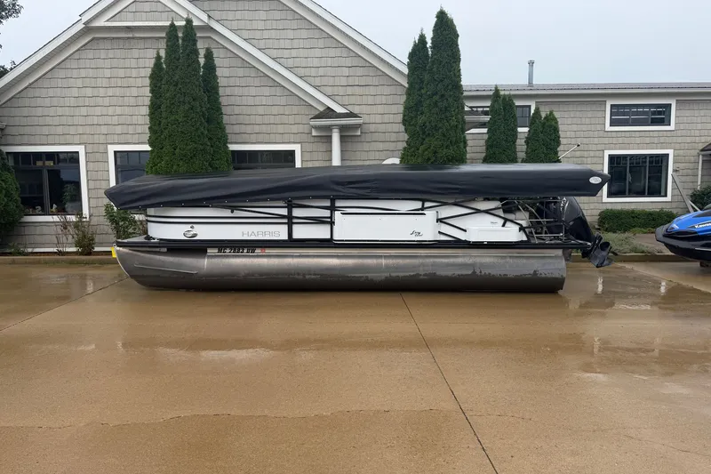 Slide: The Image of 2023 Harris Sunliner 230 pontoon boat with cover, parked on wet pavement. - 1