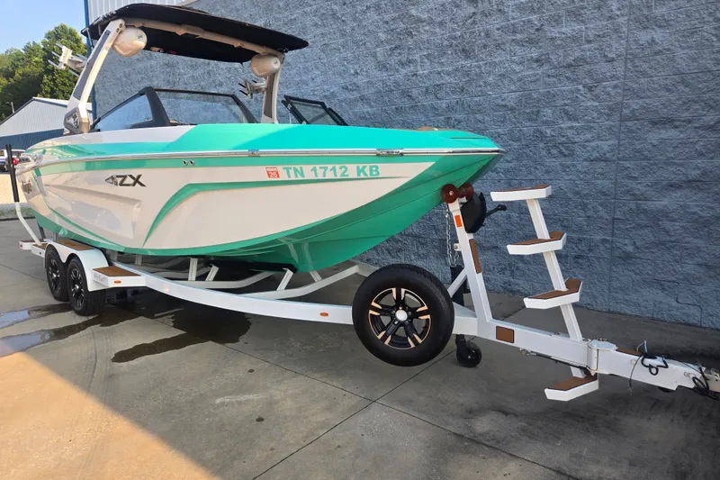 Slide: The Image of 2020 Tigé 23ZX boat on trailer, teal and white design, parked outdoors. - 3