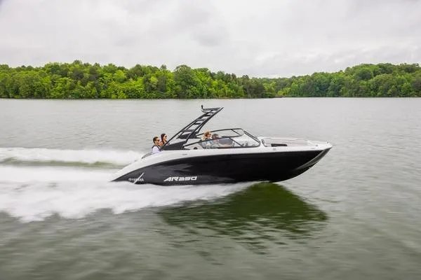 The Image of 2026 Yamaha AR250 boat speeding on a lake with lush green trees in the background. - 2