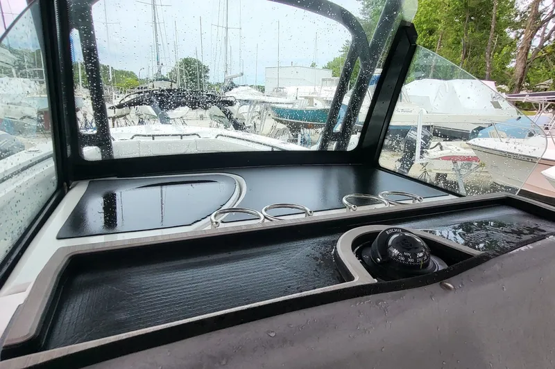 Slide: The Image of 2023 Wellcraft 302 Fisherman dashboard with compass, cup holders, and rain-soaked windshield. - 11