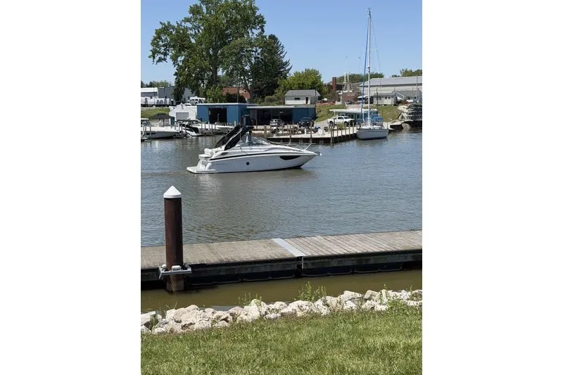The Image of 2024 Regal 28 Express boat cruising in a marina with docks and trees. - 2