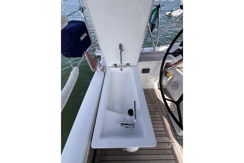 Slide: The Image of 2020 Hanse 458 yacht cockpit sink with faucet, open lid, and steering wheel visible. - 28