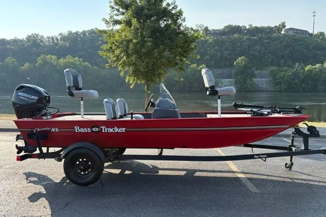 The Image of Red 2027 Tracker Bass Tracker Classic XL boat on trailer by a river. - 0