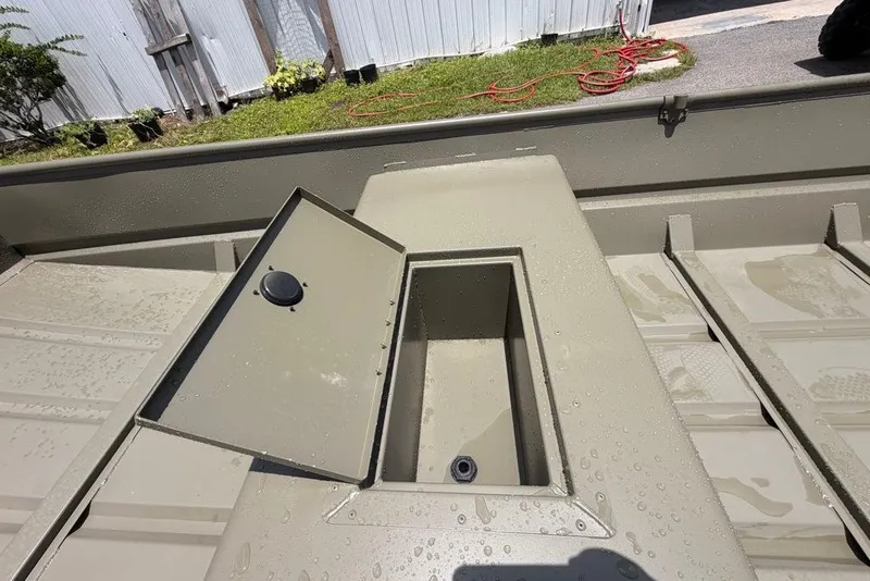 Slide: The Image of 2027 Tracker Grizzly 15 Jon boat interior with open storage compartment, wet surface. - 23