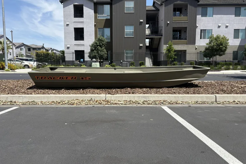 The Image of 2027 Tracker Grizzly 15 Jon boat displayed outdoors near modern apartment buildings. - 0