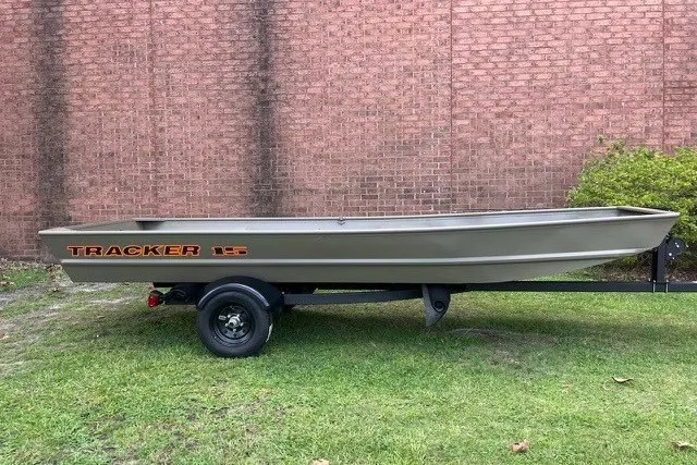 The Image of 2027 Tracker Grizzly 15 Jon boat on trailer, parked on grass by brick wall. - 0