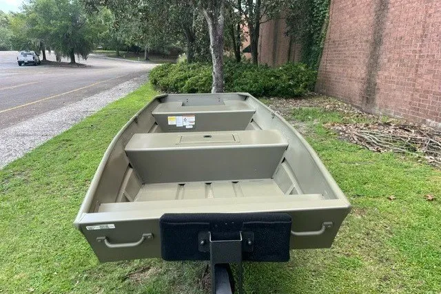 Slide: The Image of 2027 Tracker Grizzly 15 Jon boat on grass near a brick wall and trees. - 28