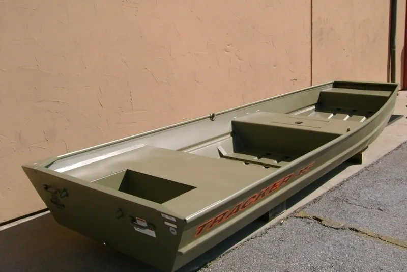 The Image of A green Tracker Grizzly 15 Jon boat sits on a concrete floor next to a wall. - 0