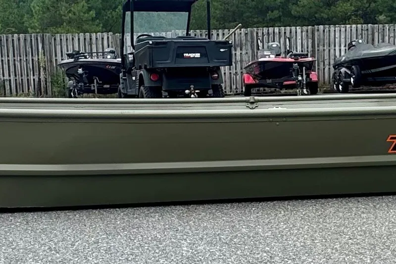 The Image of 2027 Tracker Grizzly 15 Jon boat parked outdoors with other boats and a utility vehicle. - 0
