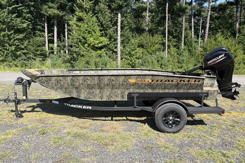 The Image of 2027 Tracker Grizzly 1553 Timber boat on trailer, camo design, parked outdoors. - 0