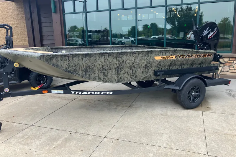 The Image of 2027 Tracker Grizzly 1553 Timber boat on trailer, camo design, parked outdoors. - 0