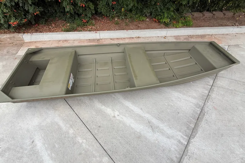 The Image of 2027 Tracker Grizzly 15 Jon boat on concrete, surrounded by greenery. - 0