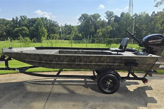 The Image of 2027 Tracker Grizzly 1654 T Sportsman boat on trailer, outdoors with lush greenery background. - 0