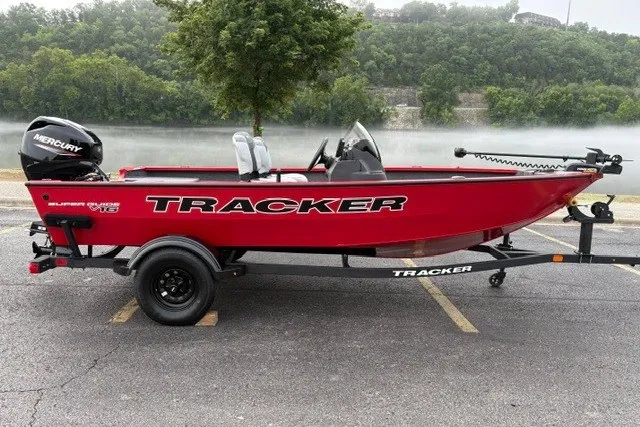 The Image of Red 2027 Tracker Super Guide V-16 SC boat on trailer, parked near a scenic river. - 0