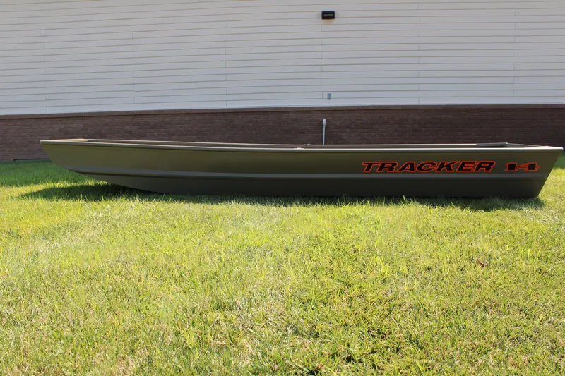 The Image of 2027 Tracker Grizzly 14 Jon boat on grass, side view, against a building backdrop. - 0