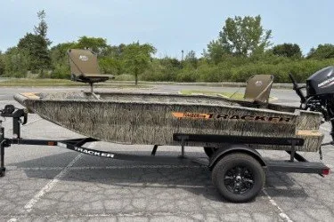 The Image of 2027 Tracker Grizzly 1553 Timber boat on trailer, camo design, parked outdoors. - 0