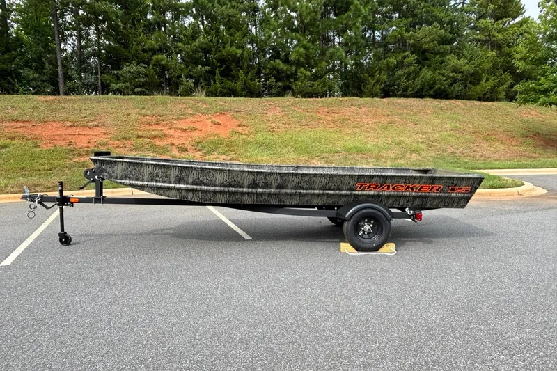 The Image of 2027 Tracker Grizzly 15 Jon boat on trailer, parked on asphalt near grassy hill. - 0