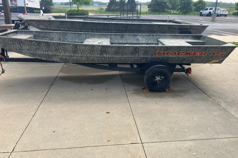 The Image of 2027 Tracker Grizzly 15 Jon boat on trailer, camo design, parked outdoors. - 0