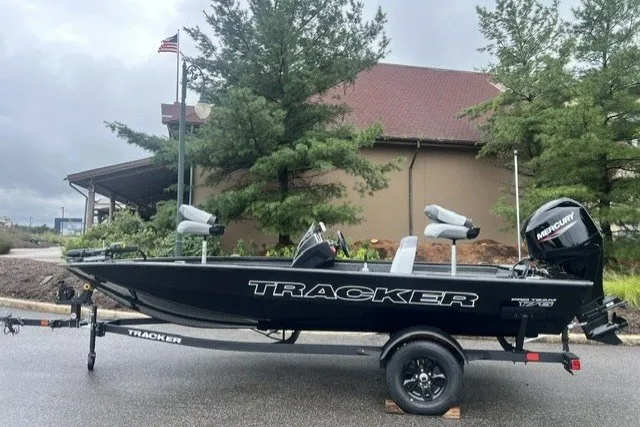 The Image of 2027 Tracker Pro Team 175 boat on trailer, parked outdoors near trees and building. - 0