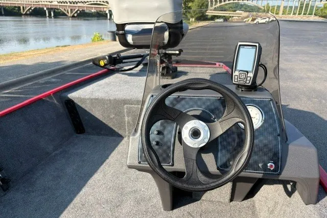 Slide: The Image of 2027 Tracker Bass Tracker Classic XL boat dashboard with steering wheel and fish finder by a river. - 16
