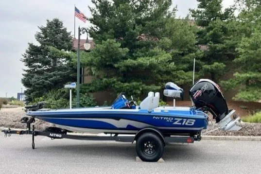 The Image of 2027 Nitro Z18 XL boat on trailer, parked outdoors with trees and American flag in background. - 0