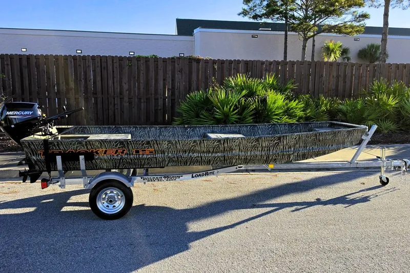 The Image of 2027 Tracker Grizzly 15 Jon boat on trailer, featuring camouflage design and Mercury outboard motor. - 0