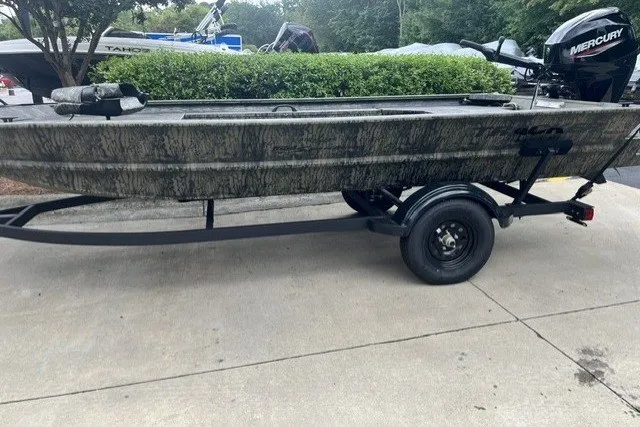 The Image of 2027 Tracker Grizzly 1654 T Sportsman boat on trailer, featuring camouflage design and Mercury outboard motor. - 0