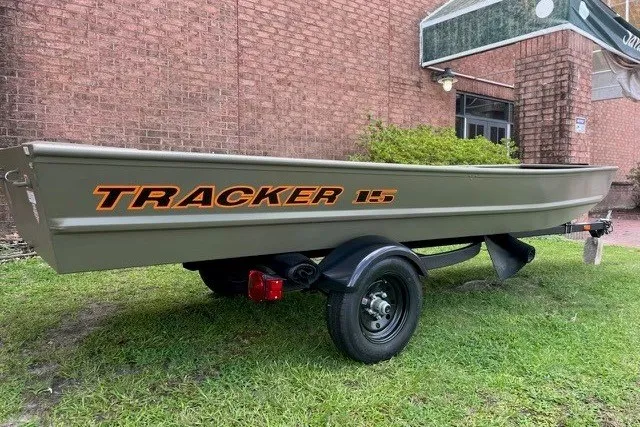 The Image of 2027 Tracker Grizzly 15 Jon boat on trailer, parked on grass near brick building. - 0