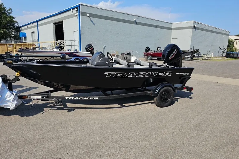 The Image of 2027 Tracker Super Guide V-16 SC boat on trailer, parked outside industrial building. - 0