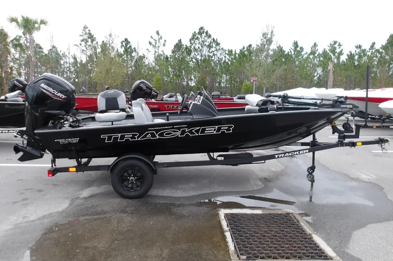 The Image of 2027 Tracker Pro Team 175 boat on trailer, parked outdoors with trees in background. - 1