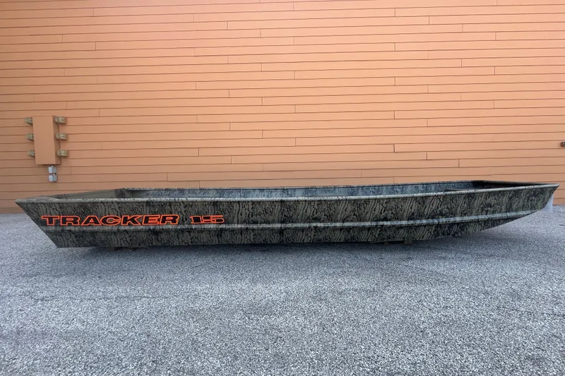 The Image of 2027 Tracker Grizzly 15 Jon boat with camouflage design against a wooden wall background. - 0