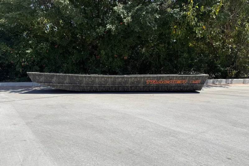 The Image of 2027 Tracker Grizzly 15 Jon boat on pavement, surrounded by lush greenery. - 0