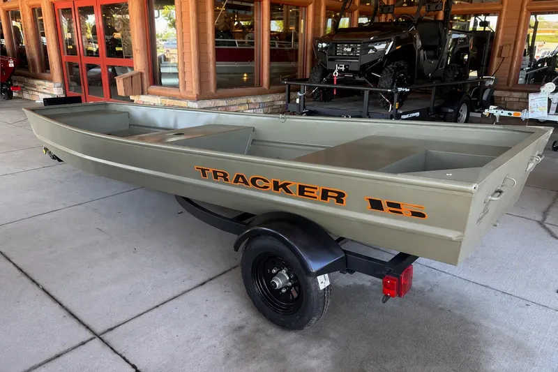 The Image of 2027 Tracker Grizzly 15 Jon boat on trailer, displayed outdoors near a wooden building. - 0