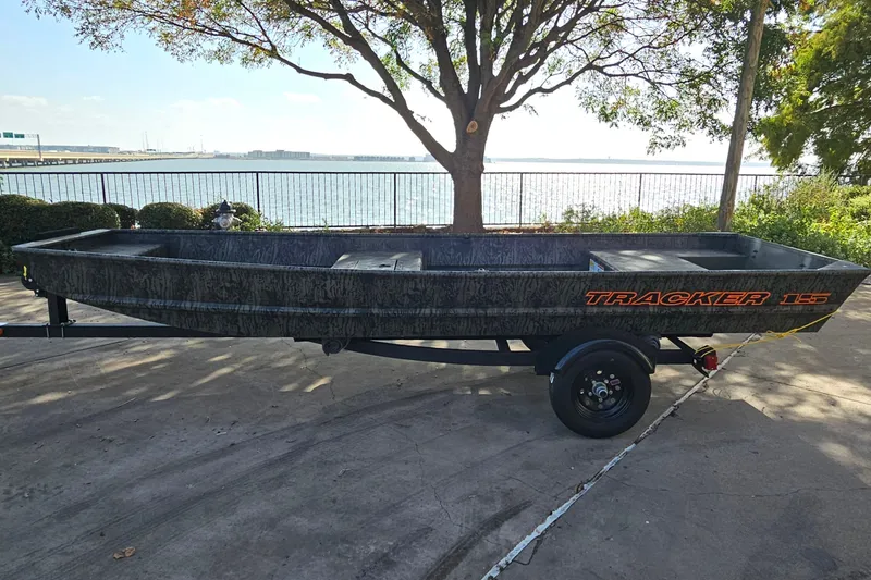 The Image of 2027 Tracker Grizzly 15 Jon boat on trailer by waterfront, under tree shade. - 0
