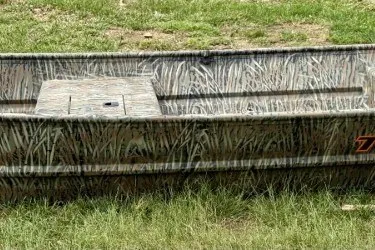 The Image of 2027 Tracker Grizzly 15 Jon boat with camouflage design on grassy terrain. - 0